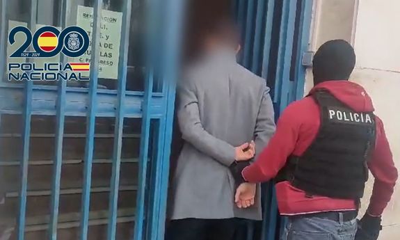 Nieumundurowany policjant prowadzi mężczyznę, który ma na ręce trzymane z tyłu założone kajdanki.