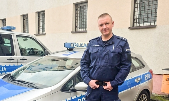 Policjant stoi przy radiowozie.