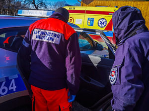 Ratownik medyczny i umundurowany policjant stoją przy radiowozie. W tle karetka pogotowia.