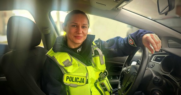Umundurowana policjantka siedzi za kierownicą radiowozu.