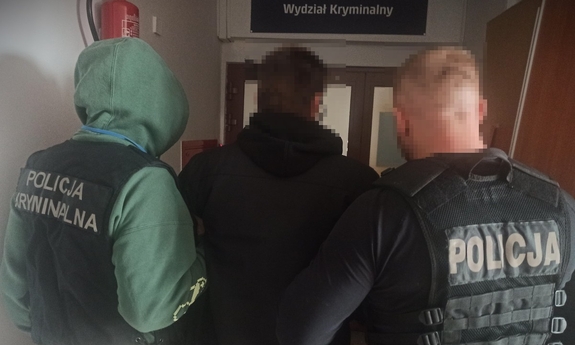 Dwaj funkcjonariusze prowadzą zatrzymanego mężczyznę.