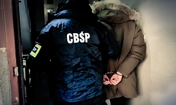 Funkcjonariusz CBŚP prowadzi zatrzymanego.
