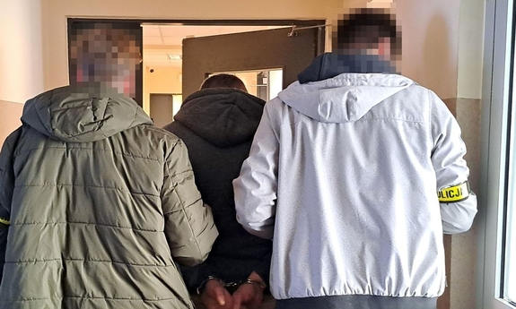 Dwaj funkcjonariusze prowadza zatrzymanego mężczyznę.