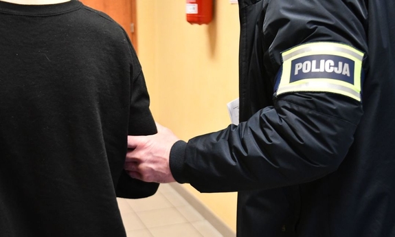 Zatrzymany za zabójstwo zakuty w kajdanki trzymany przez funkcjonariusza.