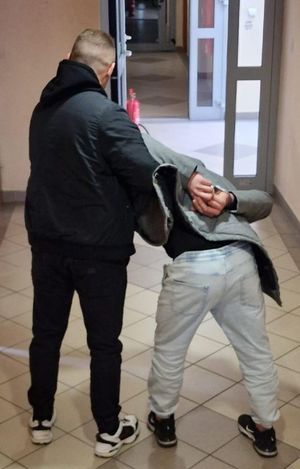 Funkcjonariusz prowadzi skutego w kajdanki mężczyznę.