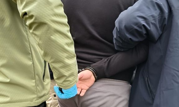 Nieumundurowani policjanci prowadzą zatrzymanego. Widok z tyłu. Widoczny fragment postaci.