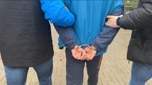 Dwaj funkcjonariusze trzymają zatrzymanego zakutego w kajdanki.