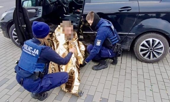 policjanci pomagają mężczyźnie leżącemu przy samochodzie.
