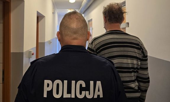 Umundurowany policjant prowadzi zatrzymanego. Widok z tyłu.