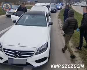 Grupa mężczyzn przy białym  samochodzie.