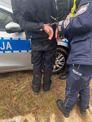 Policjant z zatrzymanym przy radiowozie.