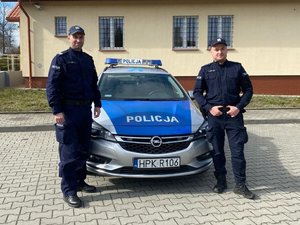 dwóch policjantów stoi przed radiowozem.