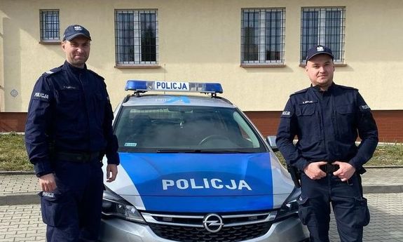 dwóch policjantów stoi przed radiowozem.