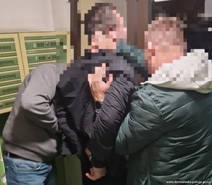 Na zdjęciu dwóch policjantów wyprowadza z klatki zatrzymanego mężczyznę w kajdankach.