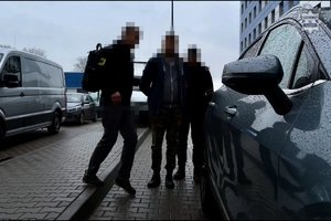 Dwaj nieumundurowani policjanci prowadzą zatrzymanego do samochodu.