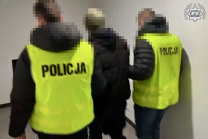 Dwaj policjanci w żółtych kamizelkach z napisem Policja prowadzą zatrzymanego.