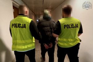 Dwaj policjanci w żółtych kamizelkach z napisem Policja prowadzą zatrzymanego.