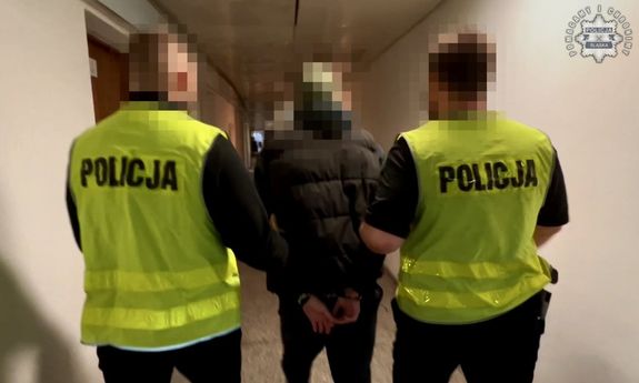Dwaj policjanci w żółtych kamizelkach prowadzą zatrzymanego.