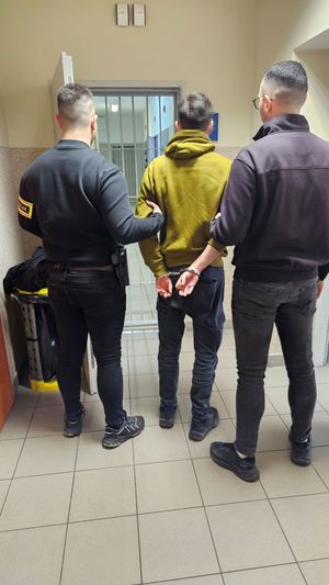 Dwaj funkcjonariusze prowadzą zatrzymanego.
