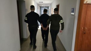 Dwaj funkcjonariusze prowadzą zatrzymanego.