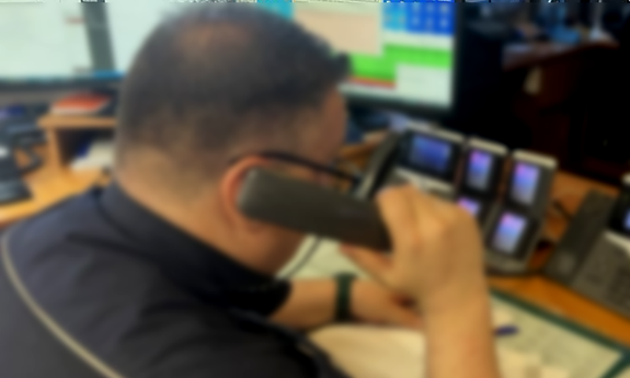 Policjant dyżurny przy biurku rozmawia przez telefon.