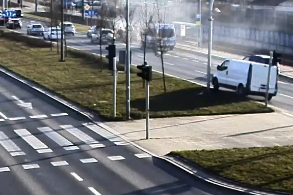 Zrzut ekranu z klatką z monitoringu na której widać ulicę, jadące auta i w oddali to, które się zapaliło.