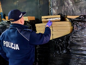 Policjant w mundurze otwierający pudełko z papierosami.