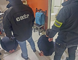 Policjanci stoją zatrzymanych mężczyzn siedzących na podłodze.