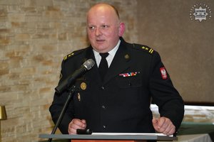 Umundurowany funkcjonariusz straży pożarnej przemawia stojąc przy mównicy.