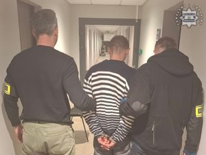 Dwaj nieumundurowani policjanci trzymają zatrzymanego mężczyznę.