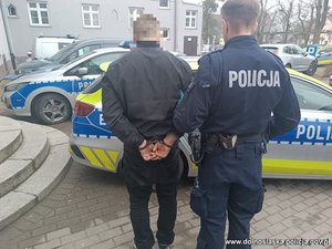 Policjant z zatrzymanym mężczyzna zakutym w kajdanki.