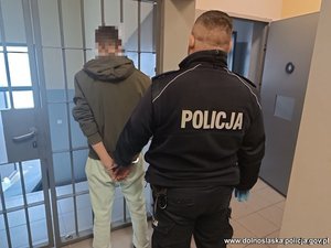 Policjant z zatrzymanym mężczyzna zakutym w kajdanki.