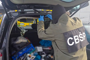 Policjant CBŚP stoi przed otwartym bagażnikiem samochodu.