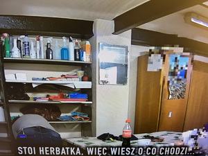 Stopklatka z nagrania ukrytej kamery. Regał z ze środkami czystości, obok niego kobieta.