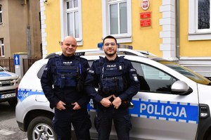 Dwaj policjanci stoją przy radiowozie.