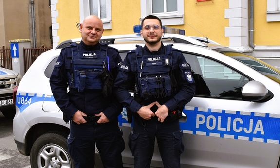 Dwaj policjanci stoją przy radiowozie.