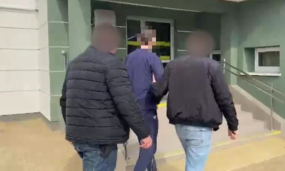 Dwaj nieumundurowani policjanci prowadzą do budynku zatrzymanego.