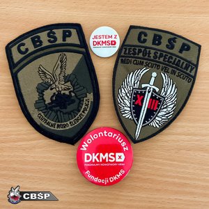 Dwie odznaki CBŚP i przypinka DKMS na stole.