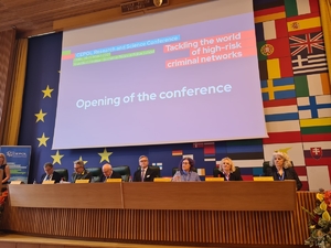 Uczestnicy konferencji siedzą przy stole. Na ścianie za nimi znajduje się ekran, na którym wyświetlana jest prezentacja.