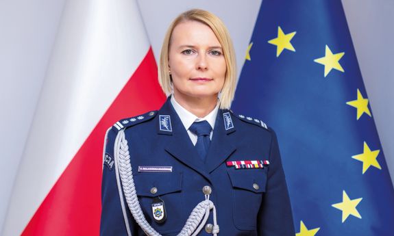 komendant rektor Akademii Policji w Szczytnie insp. dr Agata Malasińska-Nagórny stoi na tle dwóch flag, polskiej i unii europejskiej.