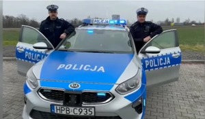 policjanci stojący po obu stronach radiowozu