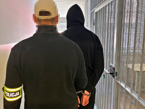 Na zdjęciu policjant prowadzi zatrzymanego mężczyznę do pomieszczenia dla osadzonych.