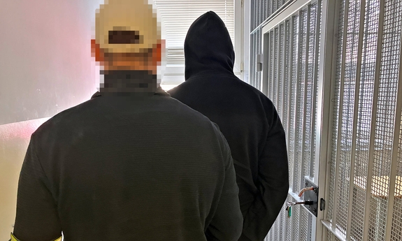 Na zdjęciu policjant prowadzi zatrzymanego mężczyznę do pomieszczenia dla osadzonych.
