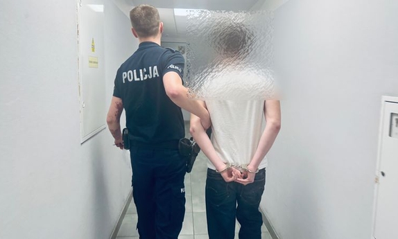 Policjant prowadzi korytarzem zatrzymanego.