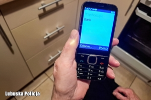 Trzymany w dłoni telefon komórkowy, na którego wyświetlaczu widać połączenie przychodzące z banku.