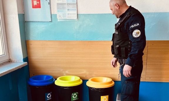 Policjant stoi przy kubłach na śmieci na szkolnym korytarzu.