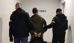 Dwaj funkcjonariusze prowadza zatrzymanego.