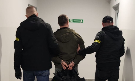 Zatrzymany mężczyzna prowadzony przez dwóch policjantów.