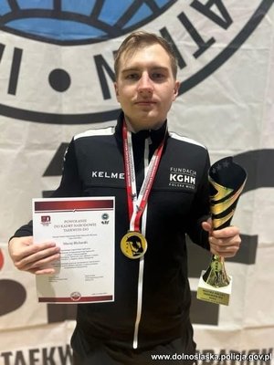 Mężczyzna trzyma puchar i dyplom, a na szyi i medal,