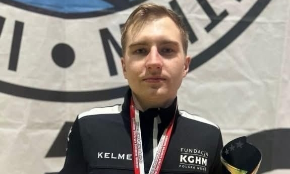 Mężczyzna trzyma puchar i dyplom, a na szyi i medal,